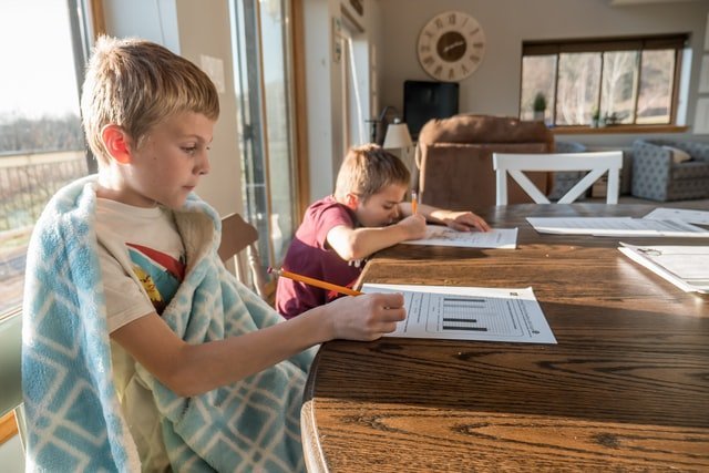two boys sitting at the table writing on a piece of paper